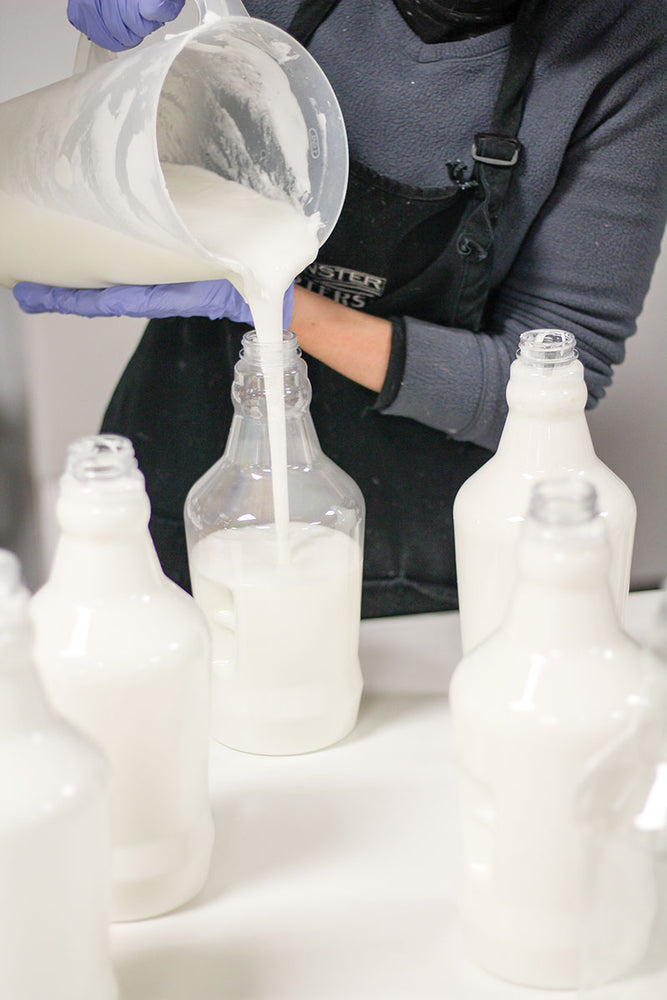 woman pouring white body butter into large 64oz  jugs 