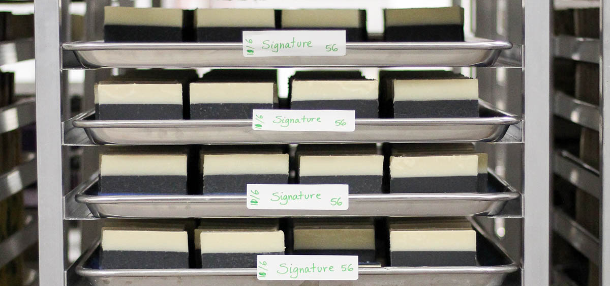 A silver rack showing 4 trays full of black and white bars of soap. Trays have stickers with the word Signature and the number 56 hand written.
