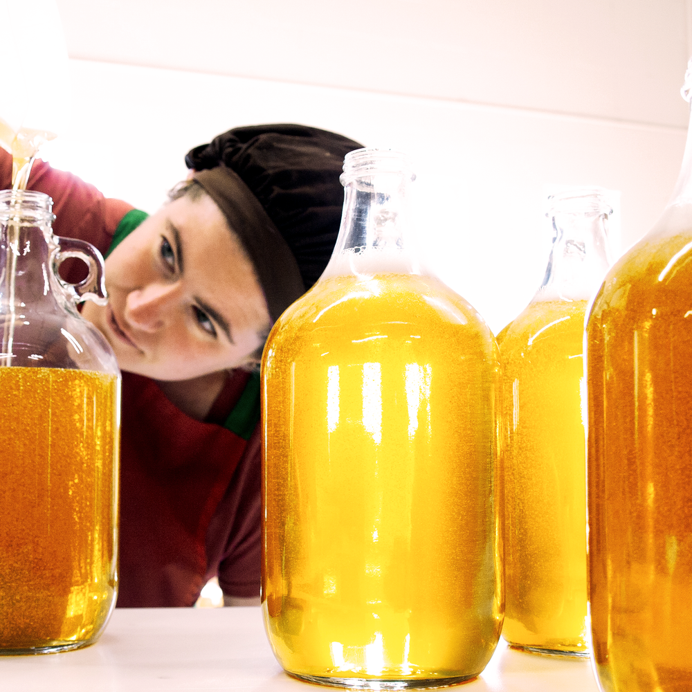 Woman pouring amber colored liquid soap into 64oz bulk glass jugs