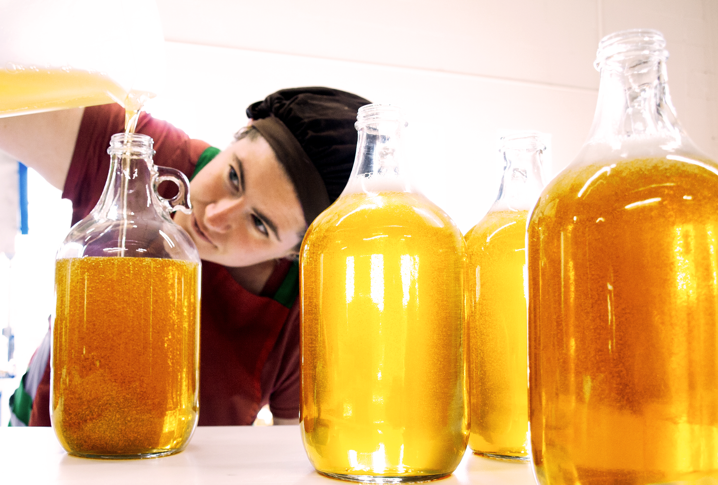 Woman pouring amber colored liquid soap into 64oz bulk glass jugs
